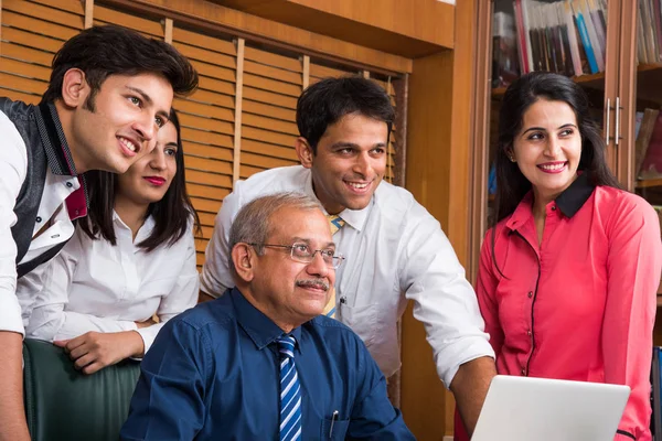 Satisfied with new plan. Group of four to five Indian cheerful young people and one experienced businessman looking at laptop with smile while leaning to the table in office — Stock Photo, Image