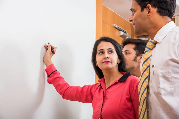 Joven empresaria india escribiendo sobre pizarra blanca con rotulador y otros empresarios que buscan — Foto de Stock