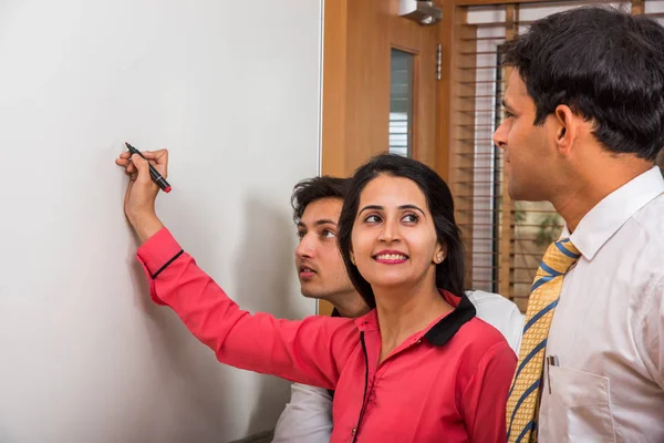 Joven empresaria india escribiendo sobre pizarra blanca con rotulador y otros empresarios que buscan — Foto de Stock