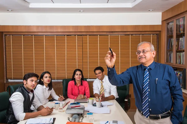 Hint üst düzey işadamı Toplantı salonunun arka planda diğer genç iş adamları süre içinde sunu pen marker ile şeffaf cam üzerine yazma