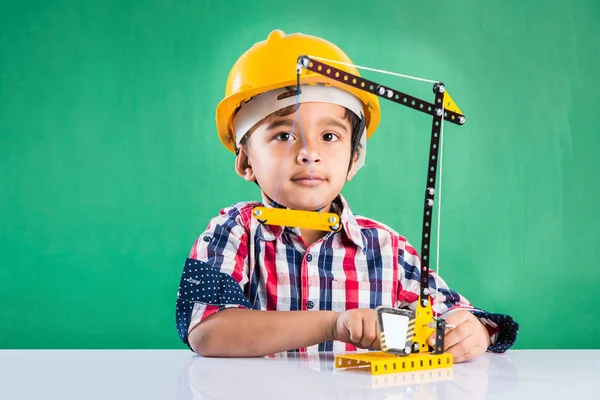 Bonito indiana bebê menino brincando com brinquedo guindaste vestindo amarelo chapéu de construção ou chapéu duro, infância e educação conceito, com rabiscos desenhados sobre quadro verde — Fotografia de Stock