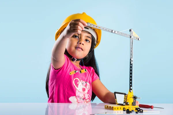 Χαριτωμένο μωρό ινδική κορίτσι παίζει με το παιχνίδι Γερανός φορώντας καπέλο κίτρινο κατασκευή ή σκληρό καπέλο, την παιδική ηλικία και την εκπαίδευση έννοια — Φωτογραφία Αρχείου