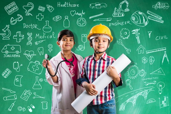 Kids and education concept - Small indian boy and girl posing in front of Green chalk board in engineers fancy dress with yellow helmet and doctor costume with stethoscope, wanna be engineer or doctor — Stock Photo, Image