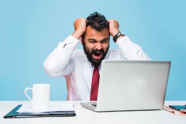 bilgisayar masasında ofiste üzücü ifadeler gösterilen sakallı sinirli Hint genç iş adamı