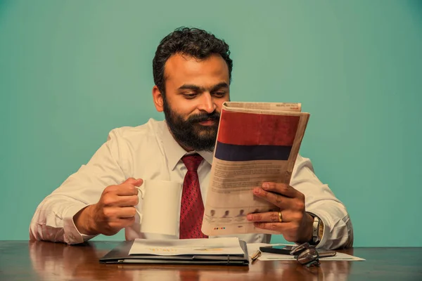 Foto com efeito especial mostrando índio jovem empresário lendo jornal enquanto toma café no escritório, asiático empresário apreciando café enquanto lê publicação de notícias — Fotografia de Stock