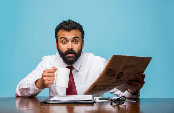 Foto con effetto speciale che mostra indiano giovane uomo d'affari leggendo giornale mentre prende il caffè in ufficio, uomo d'affari asiatico godendo il caffè durante la lettura di pubblicazione di notizie — Foto Stock