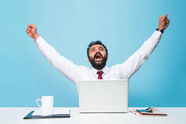 indian businessman and success or victory, indian businessman in beard showing extreme happiness with both hands stretched while sitting and looking at computer screen in the office