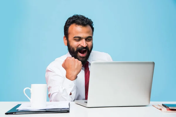 Empresario indio y éxito o victoria, empresario indio en barba mostrando felicidad extrema con ambas manos estiradas mientras se sienta y mira la pantalla de la computadora en la oficina — Foto de Stock