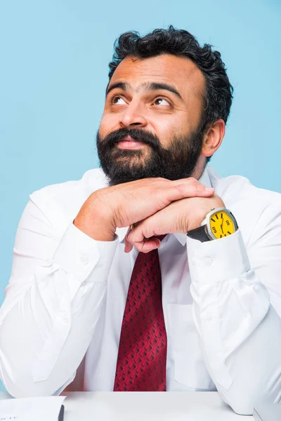 Porträtt av ung indisk affärsman i skägg, sitter i avslappnad ställning på office bord med trevlig look. Självsäker asiatisk manlig näringsidkare — Stockfoto