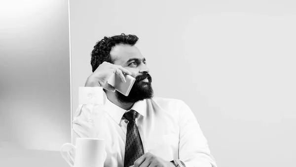 Jovem empresário indiano em barba ocupado em telefonema ao usar laptop ou computador no escritório, empresário asiático falando usando smartphone — Fotografia de Stock