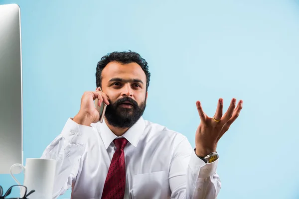 Giovane uomo d'affari indiano in barba occupato a telefonare durante l'utilizzo di laptop o computer in ufficio, uomo d'affari asiatico parlando utilizzando smartphone — Foto Stock