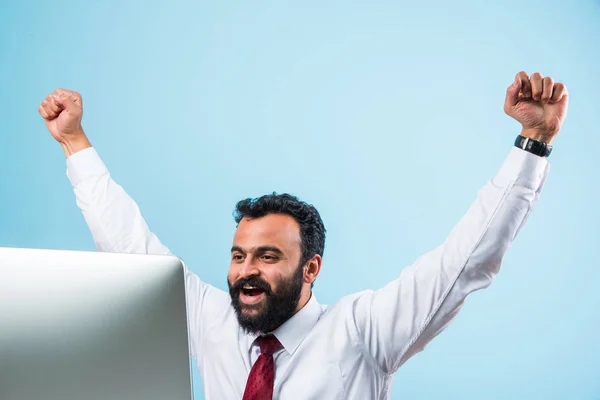 Indisk affärsman och framgång eller seger, indisk affärsman i skägg visar extrem lycka med båda händerna sträckta medan du sitter och tittar på datorskärmen på kontoret — Stockfoto