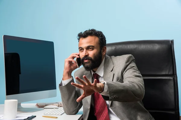 Young Indian businessman in beard busy on phone call while using laptop or computer in office, asian businessman talking using smartphone — Stock Photo, Image