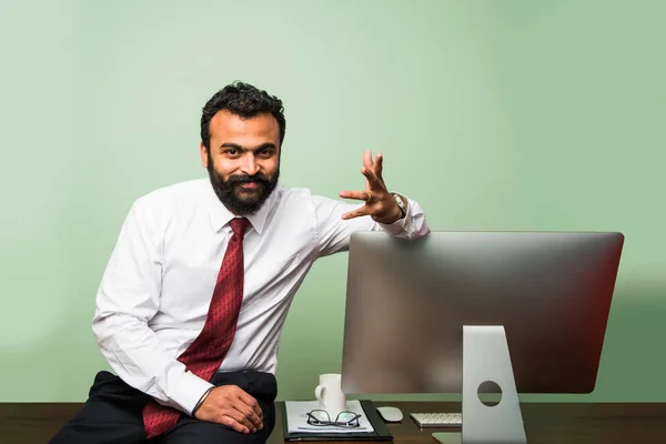 Retrato de jovem empresário indiano em barba, sentado em posição relaxada na mesa de escritório com aparência agradável. Confiante asiático homem de negócios pessoa — Fotografia de Stock