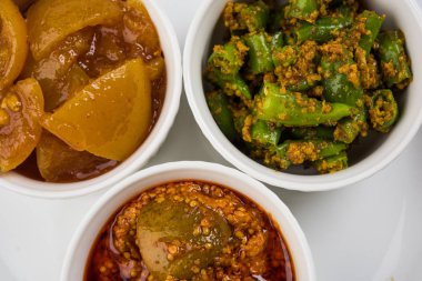 Group photograph of indian pickles like mango pickle , lemon pickle and green chilli pickle, sarved in ceramic bowls, selective focus clipart