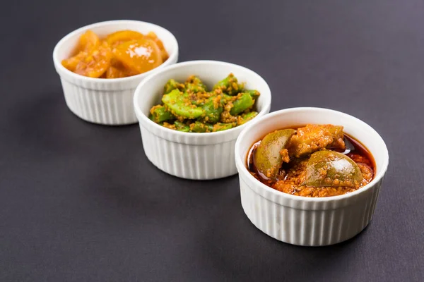 Group photograph of indian pickles like mango pickle , lemon pickle and green chilli pickle, sarved in ceramic bowls, selective focus