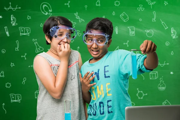 2 παιδάκια ινδική κάνει χημεία πείραμα στην τάξη με γυαλιά ασφάλειας σε μόνιμη φόντο πράσινο πίνακα κιμωλίας με doodles επιστήμη που πάνω του — Φωτογραφία Αρχείου