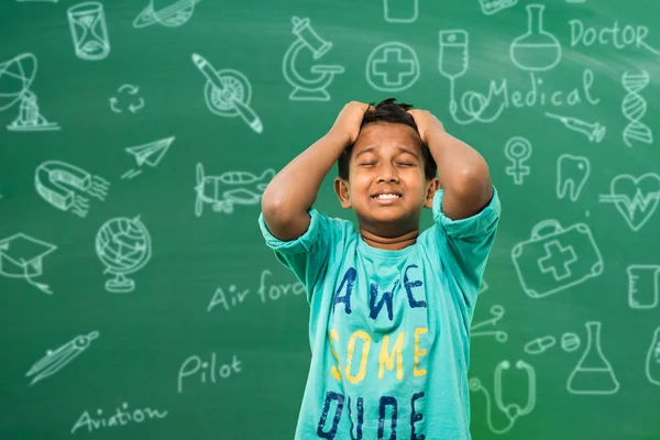 Écolier indien ou garçon tirant les cheveux dans la tristesse ou la détresse à cause de la pression de l'étude ou de la concurrence, debout isolé sur fond de tableau vert — Photo