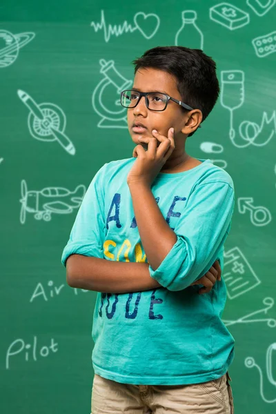 Індійська школяр або хлопчика в spectsin позі мислення, стоячи ізольованих над зеленим дошці фону з освіти каракулі — стокове фото