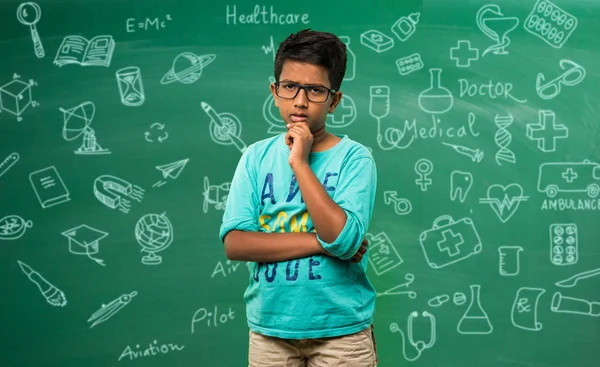 Indiana escola criança ou menino em espetáculos pensando pose, de pé isolado sobre verde quadro fundo com educação doodles — Fotografia de Stock