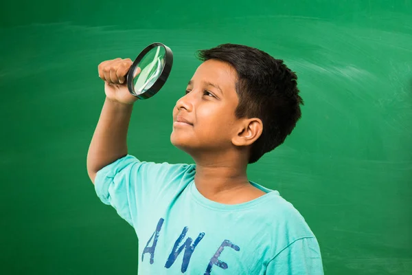 Menino indiano segurando lupa de pé isolado sobre fundo quadro verde — Fotografia de Stock