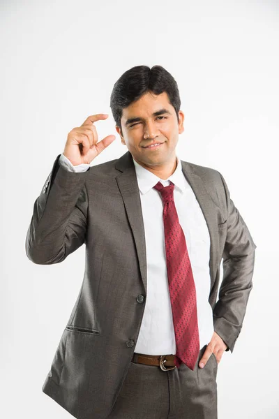 Joven empresario indio mostrando un pequeño signo de cantidad o posando como sosteniendo algo en la mano derecha frente a su rostro y cámara, aislado sobre fondo blanco — Foto de Stock