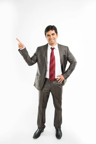 Indisk ung affärsman pekar kopia utrymme. Glad ung man i brun kostym tittar på kameran och ler medan stående mot vit bakgrund och pekar kopia utrymme — Stockfoto