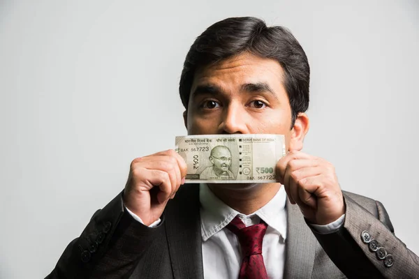 indian businessman holding indian currency note covering mouth or face and asking to keep silence or secret