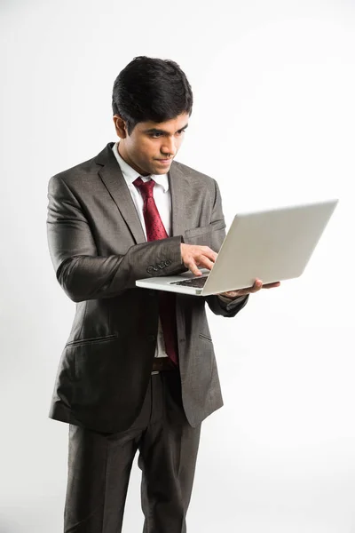 Portrait d'un jeune homme d'affaires indien confiant travaillant sur son ordinateur ou son ordinateur portable au bureau, homme d'affaires utilisant un ordinateur portable et souriant debout isolé sur fond blanc — Photo