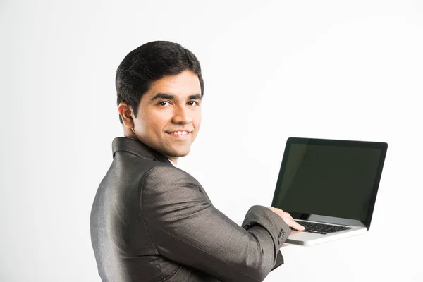 Portrait d'un jeune homme d'affaires indien confiant travaillant sur son ordinateur ou son ordinateur portable au bureau, homme d'affaires utilisant un ordinateur portable et souriant debout isolé sur fond blanc — Photo