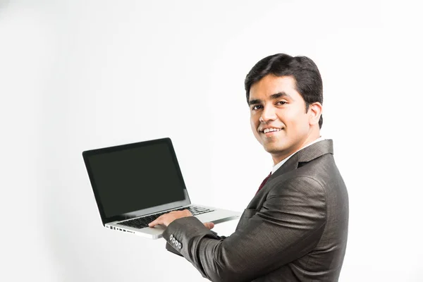 Portrait d'un jeune homme d'affaires indien confiant travaillant sur son ordinateur ou son ordinateur portable au bureau, homme d'affaires utilisant un ordinateur portable et souriant debout isolé sur fond blanc — Photo