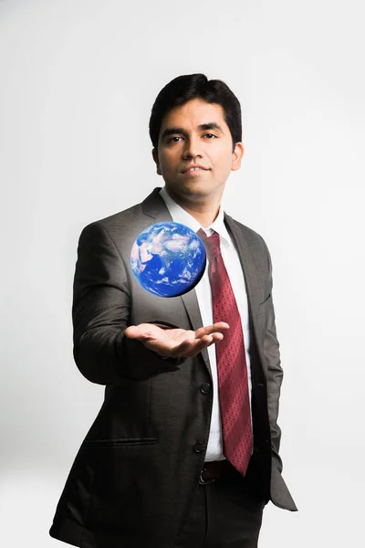 Индийский молодой бизнесмен смотрит на плавающий синий глобус или модель земли над правой ладонью в полном корпоративном платье или одежде, как костюм и галстук, изолированные на белом фоне — стоковое фото