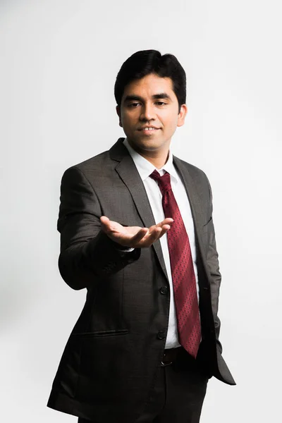 Foto completa de joven empresario indio mirando la cámara mientras equilibra algo sobre escribir la palma mirando hacia arriba y vistiendo un atuendo corporativo completo como traje y corbata, aislado sobre fondo blanco — Foto de Stock