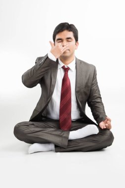 front view of an indian young businessman meditating or practicing yoga or pranayama or breathing exercise in corporate attire in the office or isolated over white background clipart