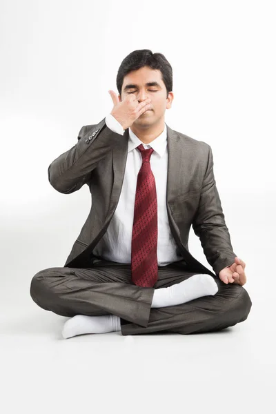 Vista frontal de um jovem empresário indiano meditando ou praticando ioga ou pranayama ou exercício de respiração em traje corporativo no escritório ou isolado sobre fundo branco — Fotografia de Stock