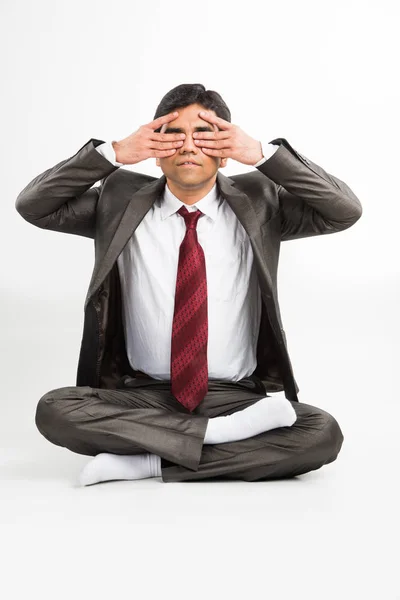 Vista frontal de un joven empresario indio meditando o practicando yoga o pranayama o ejercicio de respiración en traje corporativo en la oficina o aislado sobre fondo blanco — Foto de Stock
