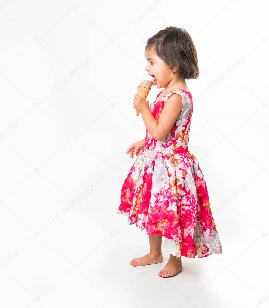indian adorable infant or girl child licking or eating chocolate ice cream in cone cone and showing happiness, isolated over white background