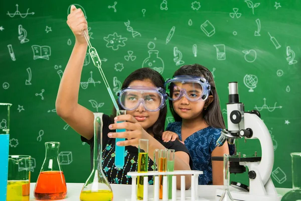 2 χαριτωμένο μικρό Ινδική κορίτσια κάνει πείραμα επιστήμης ή έργου σε μια τάξη με πράσινο πίνακα κιμωλίας έχοντας doodles επιστήμη — Φωτογραφία Αρχείου