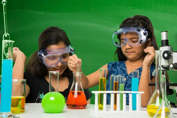 2 χαριτωμένο μικρό Ινδική κορίτσια κάνει πείραμα επιστήμης ή έργου σε μια τάξη με πράσινο πίνακα κιμωλίας έχοντας doodles επιστήμη — Φωτογραφία Αρχείου