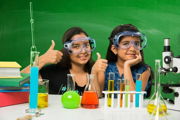 2 niñas indias lindas haciendo experimento de ciencia o proyecto en un aula con pizarra verde con garabatos de ciencia — Foto de Stock
