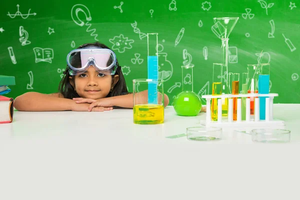 indian schoolgirl posing with science equipments like test tube, flash, beaker etc in the chemistry lab, smiling and looking at camera with green chalkboard background with science doodles