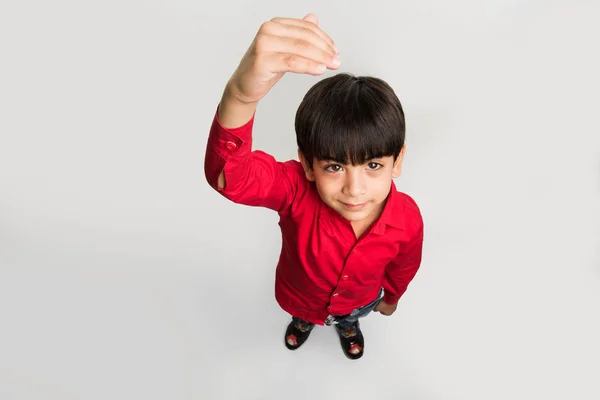 Indian smart kid or boy standing over white background and showing or measuring his height with hands, looking upwards at camera, top view — Stock Photo, Image