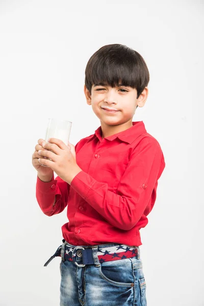 Niedlicher kleiner indischer Junge, der normale Milch trinkt oder ein Glas voll Milch vor weißem Hintergrund hält — Stockfoto