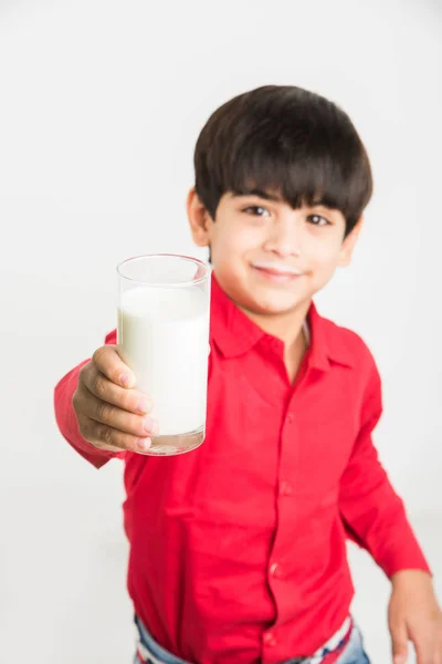 Милий маленький індійський хлопчик п'є звичайне молоко або тримає склянку повну молока, на білому тлі — стокове фото
