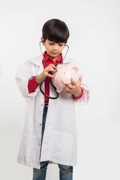 Indiase schattige jongen of jongen in doctor's uniform met de stethoscoop en piggy bank in de hand — Stockfoto
