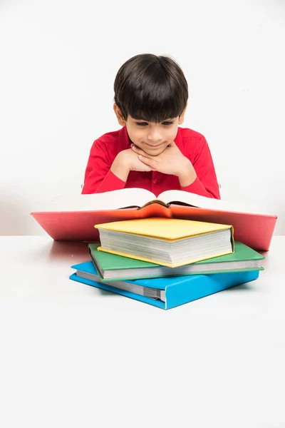 Індійський милий маленький хлопчик або дитина читає книгу над навчальним столом, ізольований на білому тлі — стокове фото