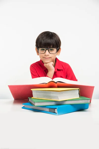 Indian cute little boy or kid reading book over study table, isolated over white background — Stock Photo, Image