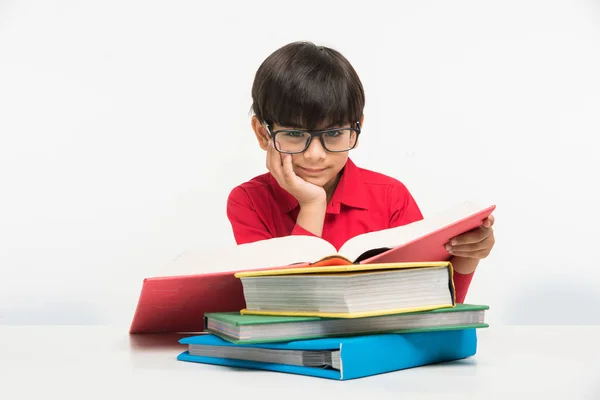 Індійський милий маленький хлопчик або дитина читає книгу над навчальним столом, ізольований на білому тлі — стокове фото