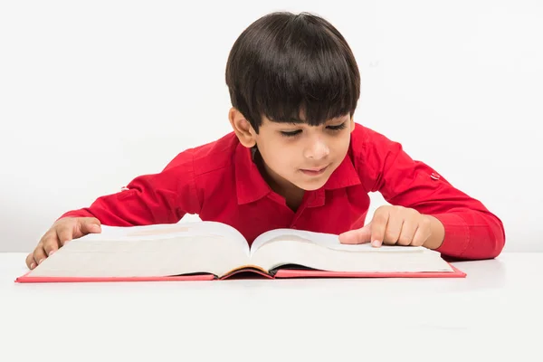 Indian cute little boy or kid reading book over study table, isolated over white background — Stock Photo, Image