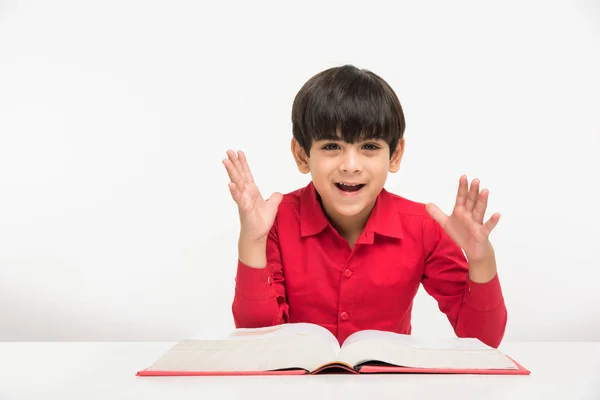 Indien mignon petit garçon ou enfant lecture livre sur table d'étude, isolé sur fond blanc — Photo